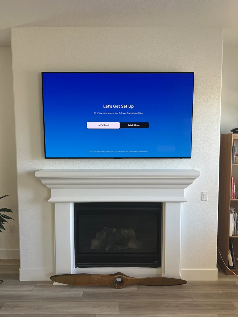 TV centered above a white fireplace mantel. No cables showing.