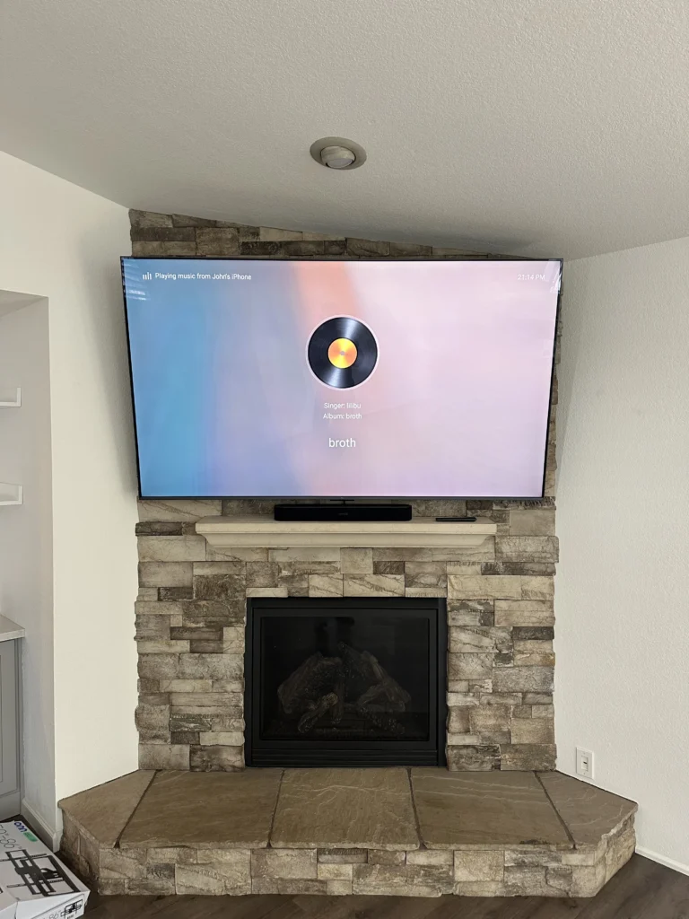 TV over a corner stone fireplace, with a soundbar on the mantel.