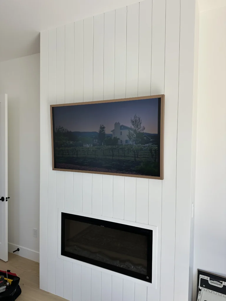 Frame TV mounted flush on a shiplap wall above a linear fireplace.